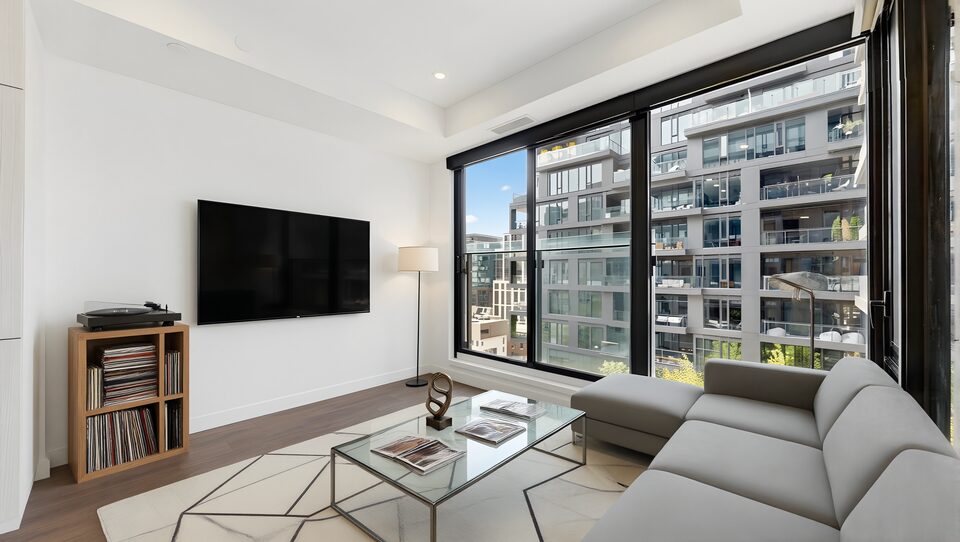 Living area virtually staged with a sofa, wall-mounted television and record player beside the windows